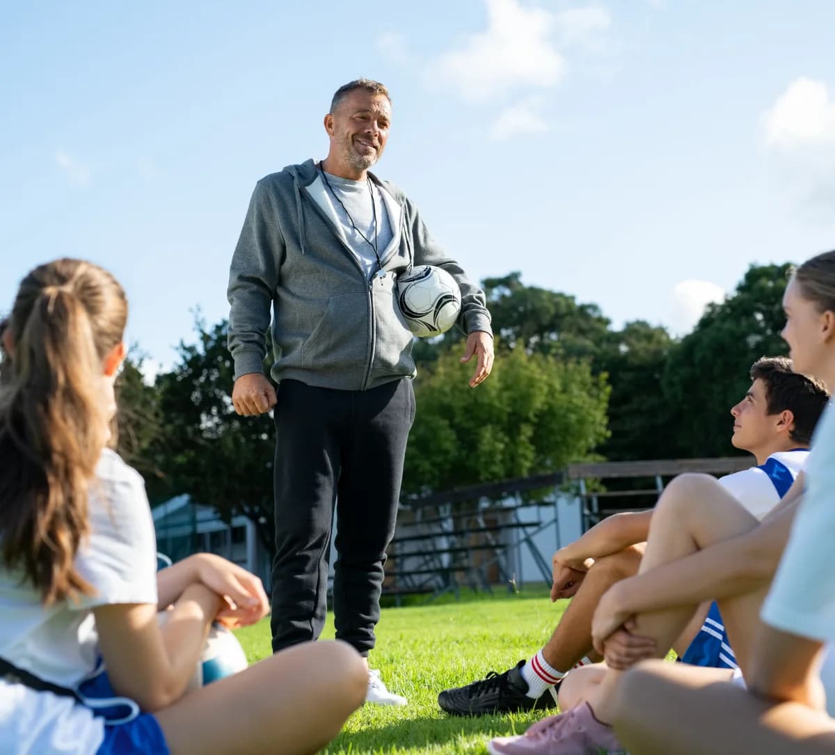 Entrenador con una pelota hablando con un grupo de futbolistas
