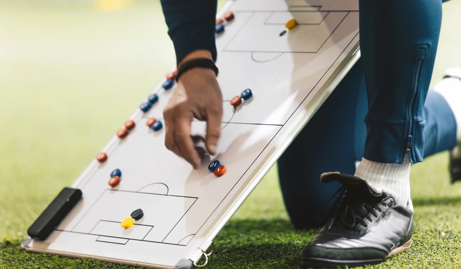 Entrenador moviendo fichas sobre una pizarra táctica de fútbol
